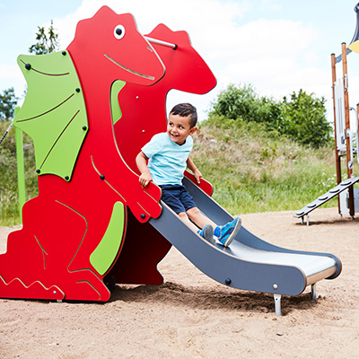 Young child slides down a small playground slide which is shaped like a red dragon.